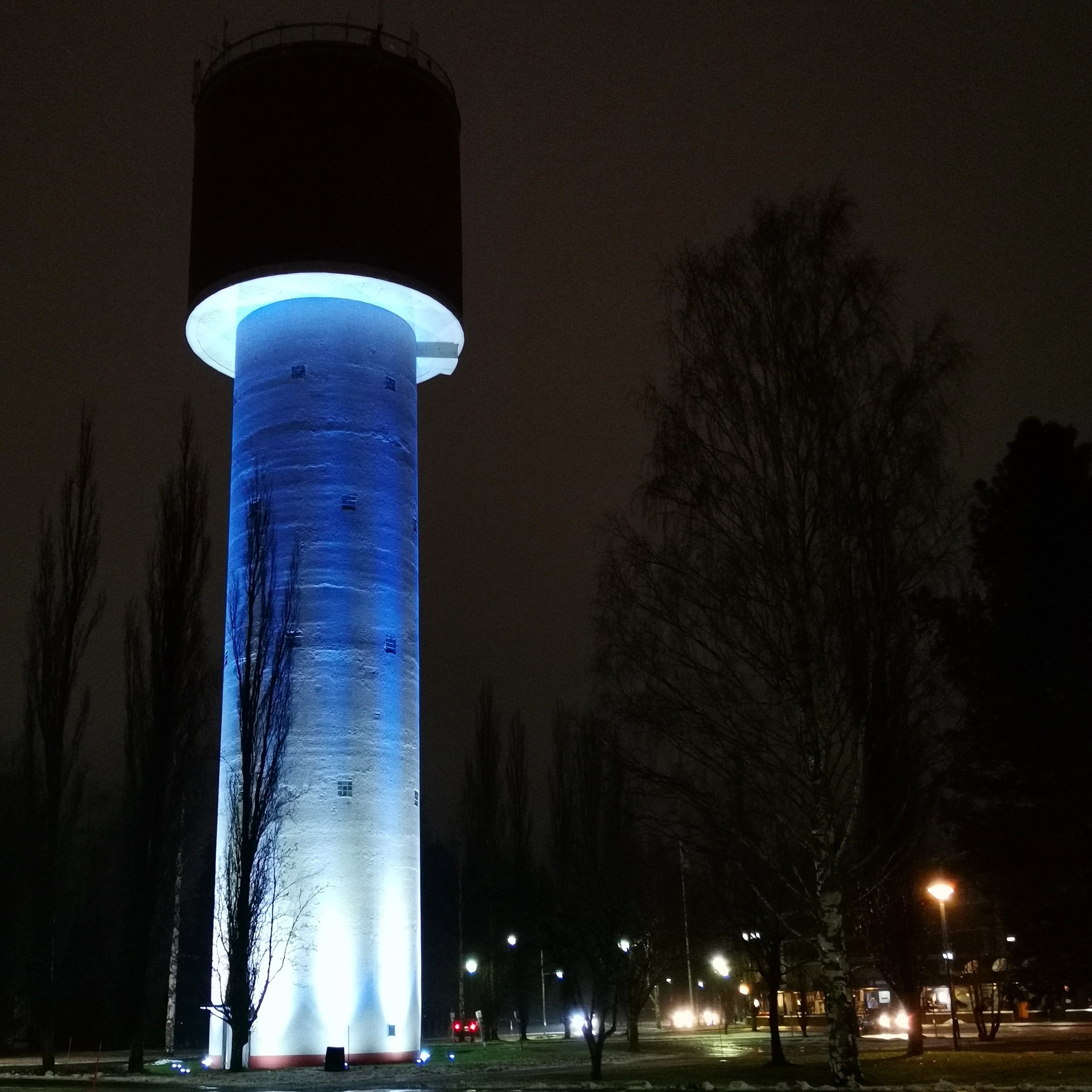 Siniseksi valaistu vesitorni pimeässä illassa.